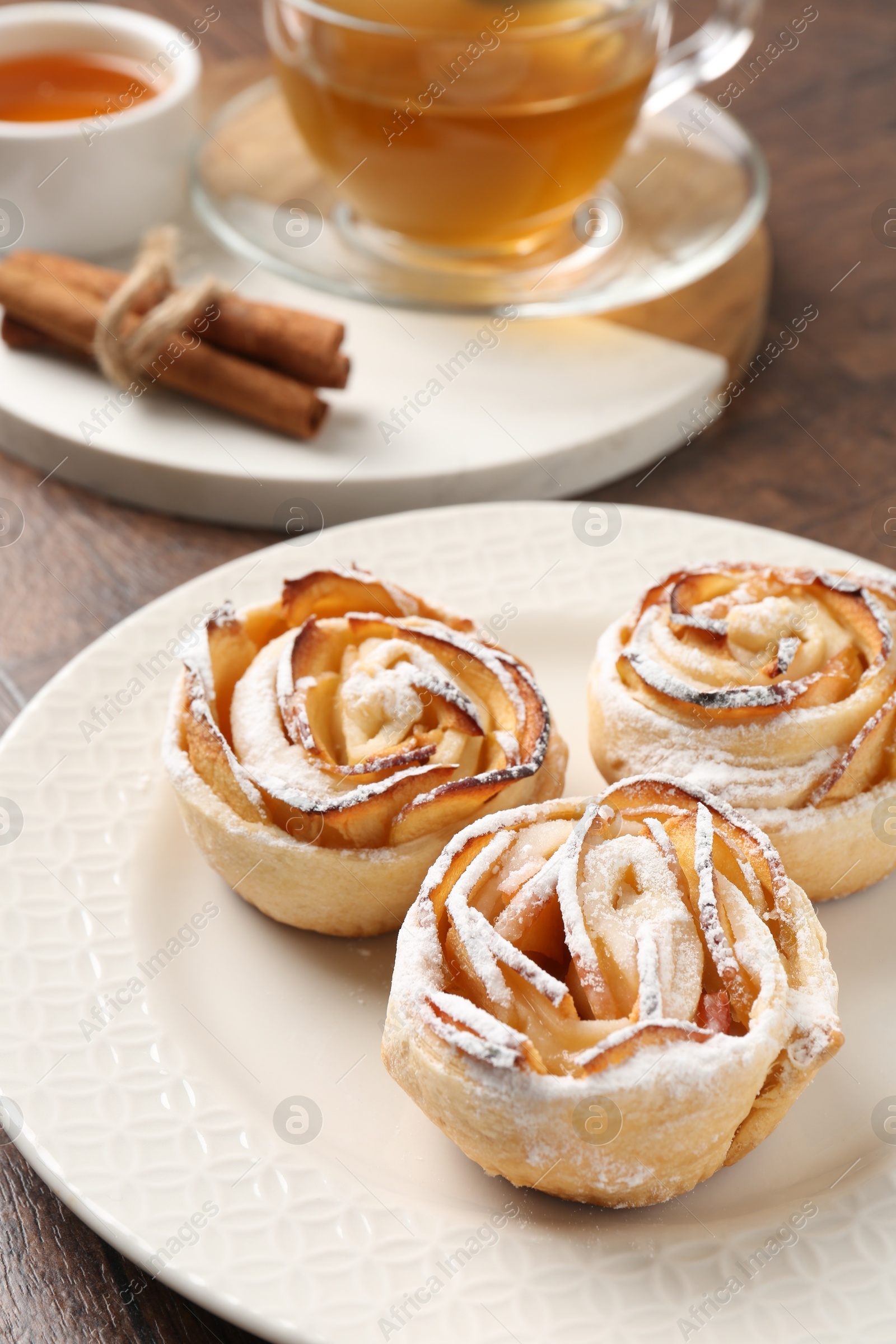 Photo of Freshly baked apple roses, honey, cinnamon sticks and tea on table, closeup