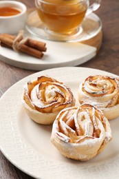 Photo of Freshly baked apple roses, honey, cinnamon sticks and tea on table, closeup