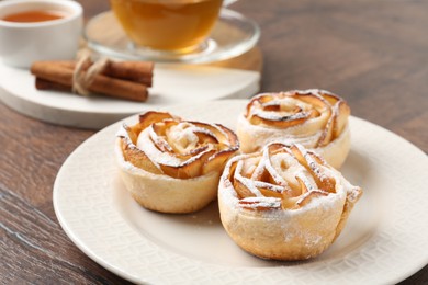 Photo of Freshly baked apple roses, honey, cinnamon sticks and tea on wooden table, closeup