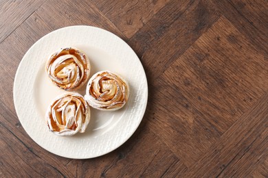 Photo of Freshly baked apple roses on wooden table, top view. Space for text