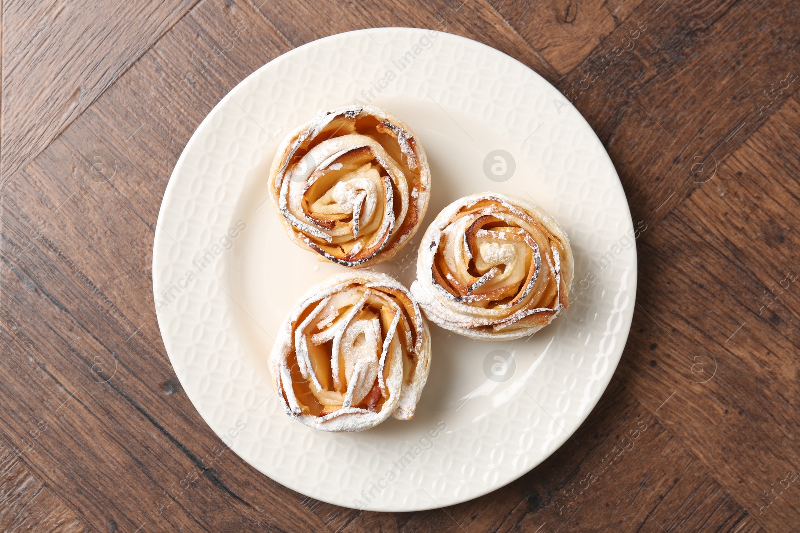Photo of Freshly baked apple roses on wooden table, top view