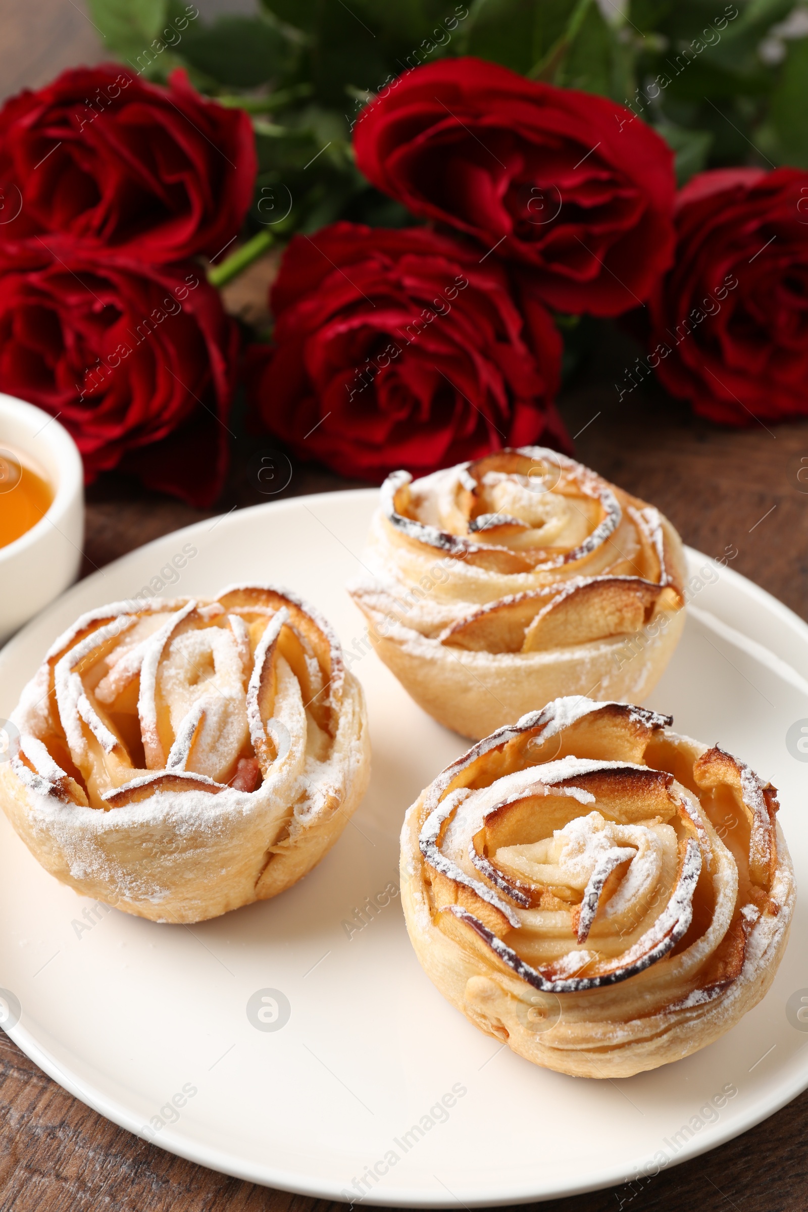 Photo of Freshly baked apple roses and beautiful flowers on table, closeup