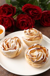 Photo of Freshly baked apple roses and beautiful flowers on table, closeup
