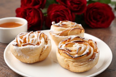 Photo of Freshly baked apple roses, honey and beautiful flowers on table, closeup