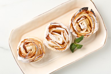 Photo of Freshly baked apple roses with mint on white marble table, top view