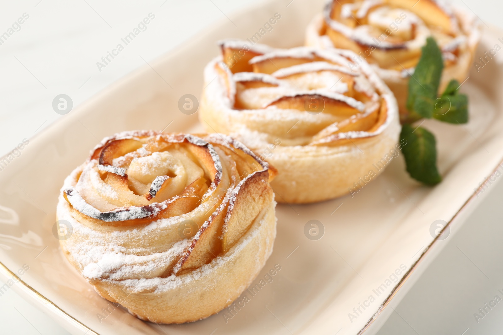 Photo of Freshly baked apple roses with mint on white table, closeup