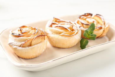 Photo of Freshly baked apple roses with mint on white table, closeup