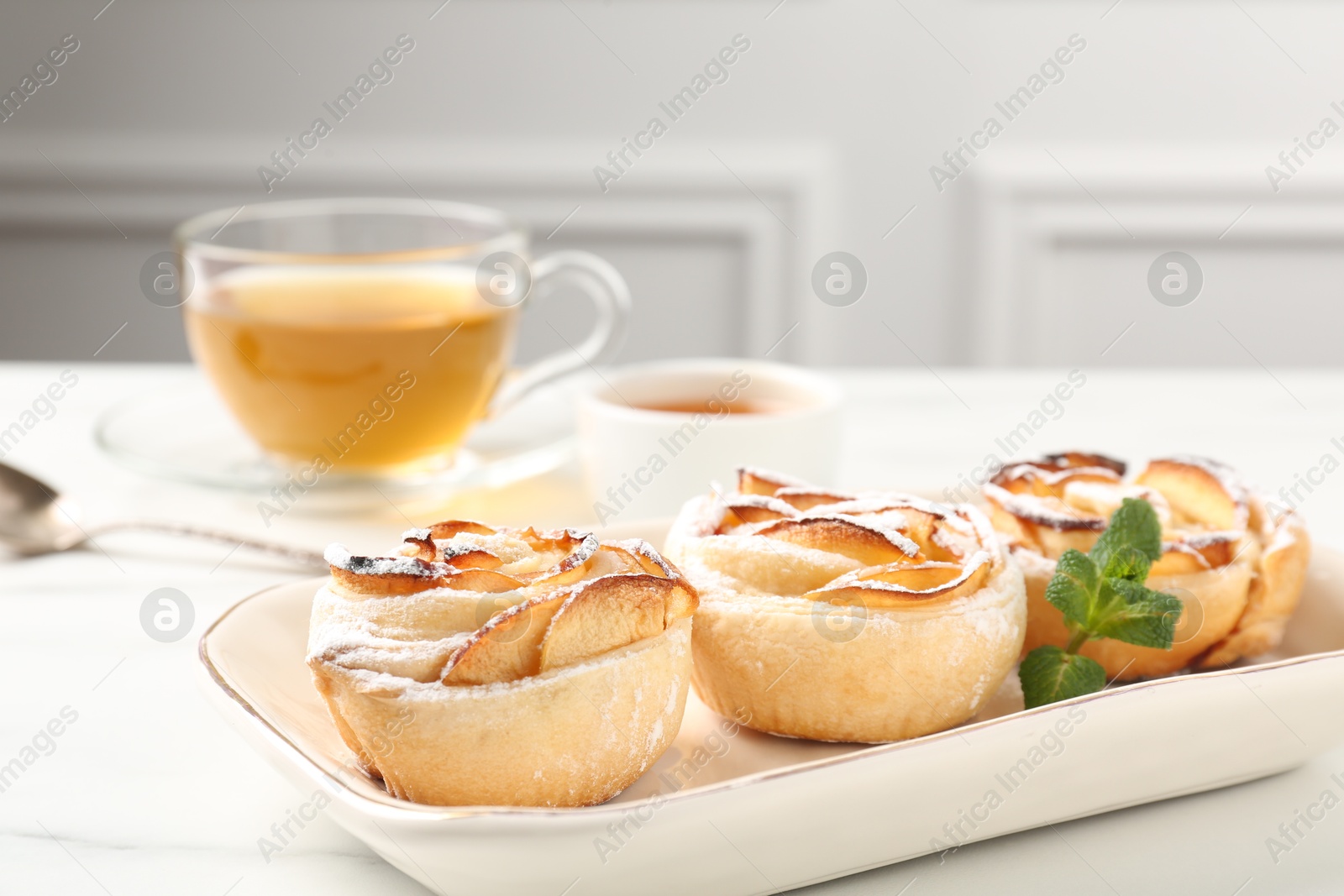 Photo of Freshly baked apple roses with mint, honey and tea on white marble table, closeup