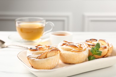 Photo of Freshly baked apple roses with mint, honey and tea on white marble table, closeup