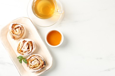 Photo of Freshly baked apple roses with mint, honey and tea on white marble table, flat lay. Space for text