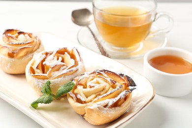 Photo of Freshly baked apple roses with mint, honey and tea on white table, closeup
