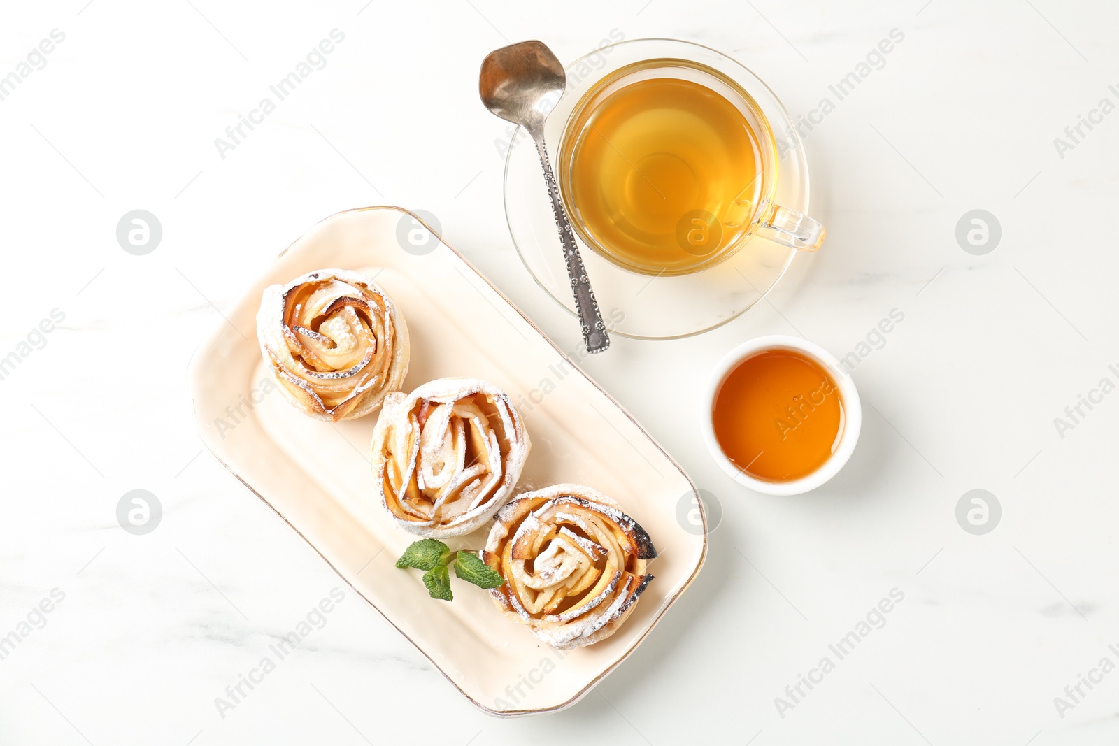 Photo of Freshly baked apple roses with mint, honey and tea on white marble table, flat lay