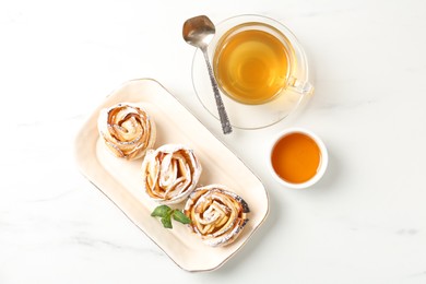Photo of Freshly baked apple roses with mint, honey and tea on white marble table, flat lay