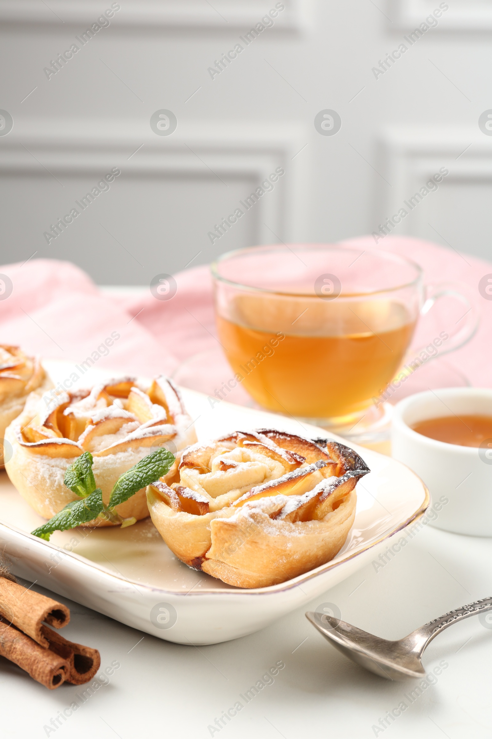 Photo of Freshly baked apple roses with mint, honey, cinnamon sticks and tea on white table, closeup