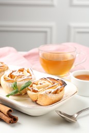 Photo of Freshly baked apple roses with mint, honey, cinnamon sticks and tea on white table, closeup