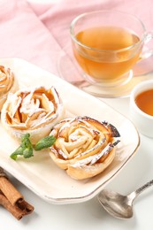 Photo of Freshly baked apple roses with mint, honey, cinnamon sticks and tea on white table, closeup