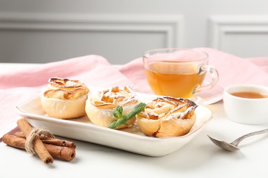 Photo of Freshly baked apple roses with mint, honey, cinnamon sticks and tea on white marble table, closeup
