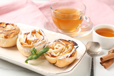 Photo of Freshly baked apple roses with mint, honey, cinnamon sticks and tea on white marble table, closeup