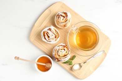 Photo of Freshly baked apple roses with mint, honey and tea on white marble table, flat lay