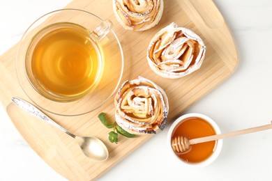 Photo of Freshly baked apple roses with mint, honey and tea on white table, flat lay