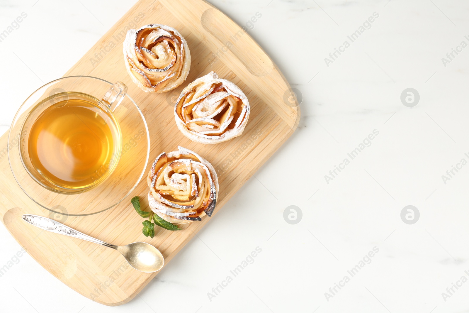 Photo of Freshly baked apple roses with mint and tea on white marble table, top view