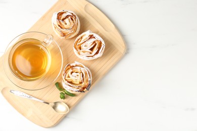 Photo of Freshly baked apple roses with mint and tea on white marble table, top view
