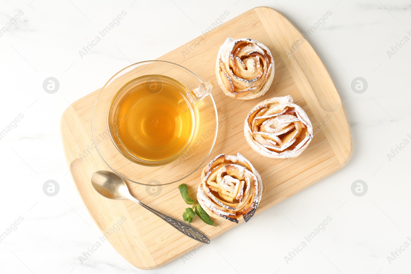 Photo of Freshly baked apple roses with mint and tea on white marble table, top view