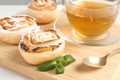 Photo of Freshly baked apple roses with mint and tea on table, closeup