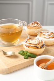 Photo of Freshly baked apple roses with mint, honey and tea on white table, closeup