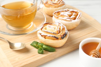 Photo of Freshly baked apple roses with mint, honey and tea on white table, closeup