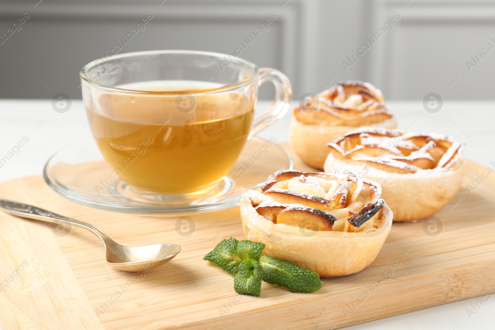 Photo of Freshly baked apple roses with mint and tea on white table, closeup