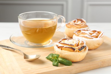 Photo of Freshly baked apple roses with mint and tea on white table, closeup