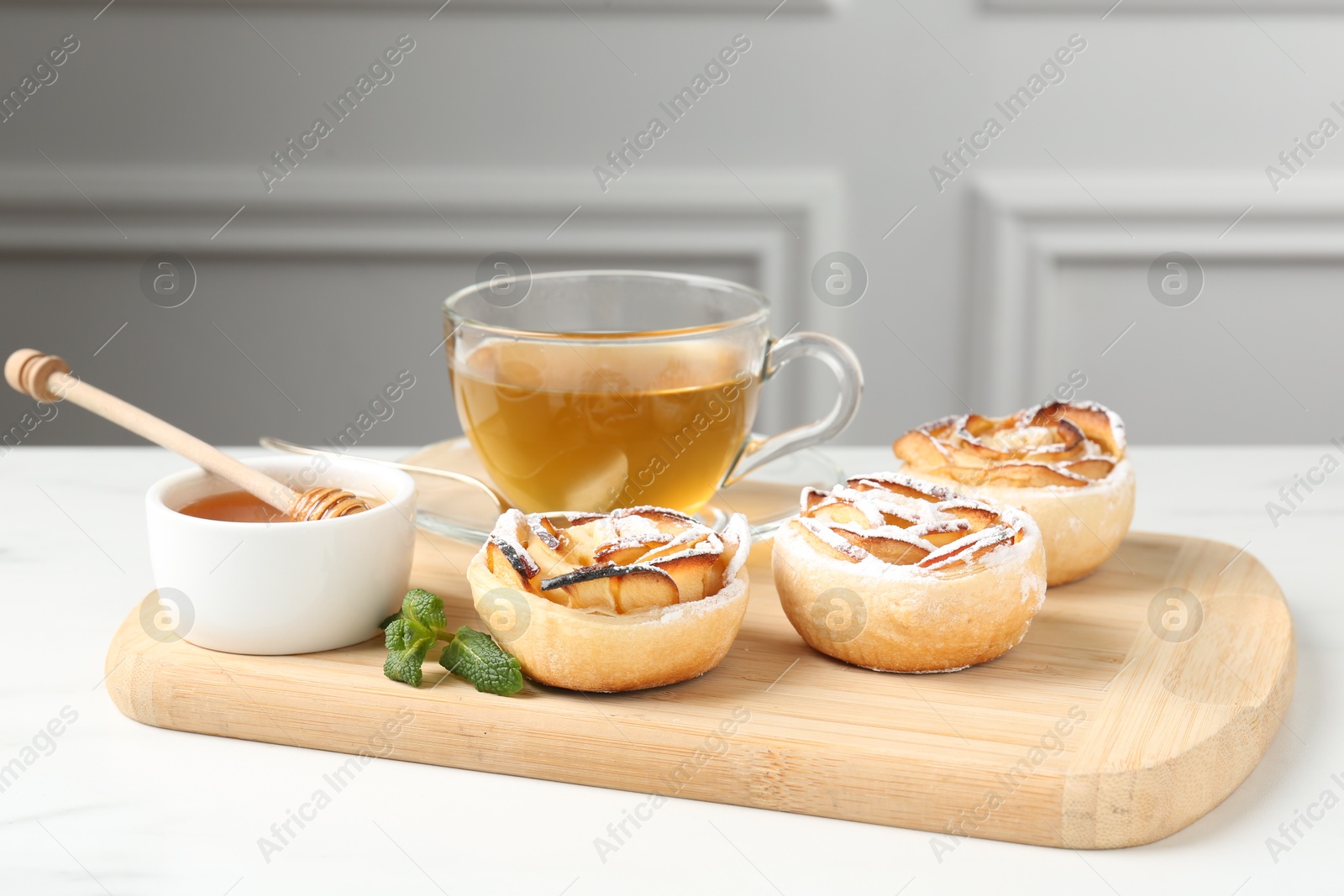 Photo of Freshly baked apple roses with mint, honey and tea on white table