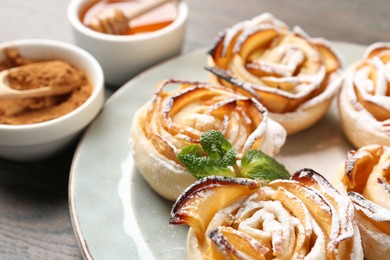 Photo of Freshly baked apple roses with mint, cocoa powder and honey on table, closeup