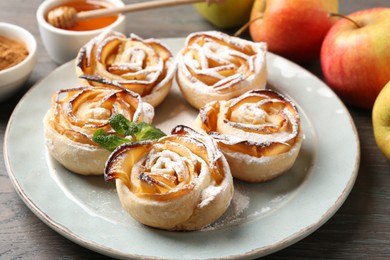 Photo of Freshly baked apple roses with mint, fruits and honey on wooden table, closeup
