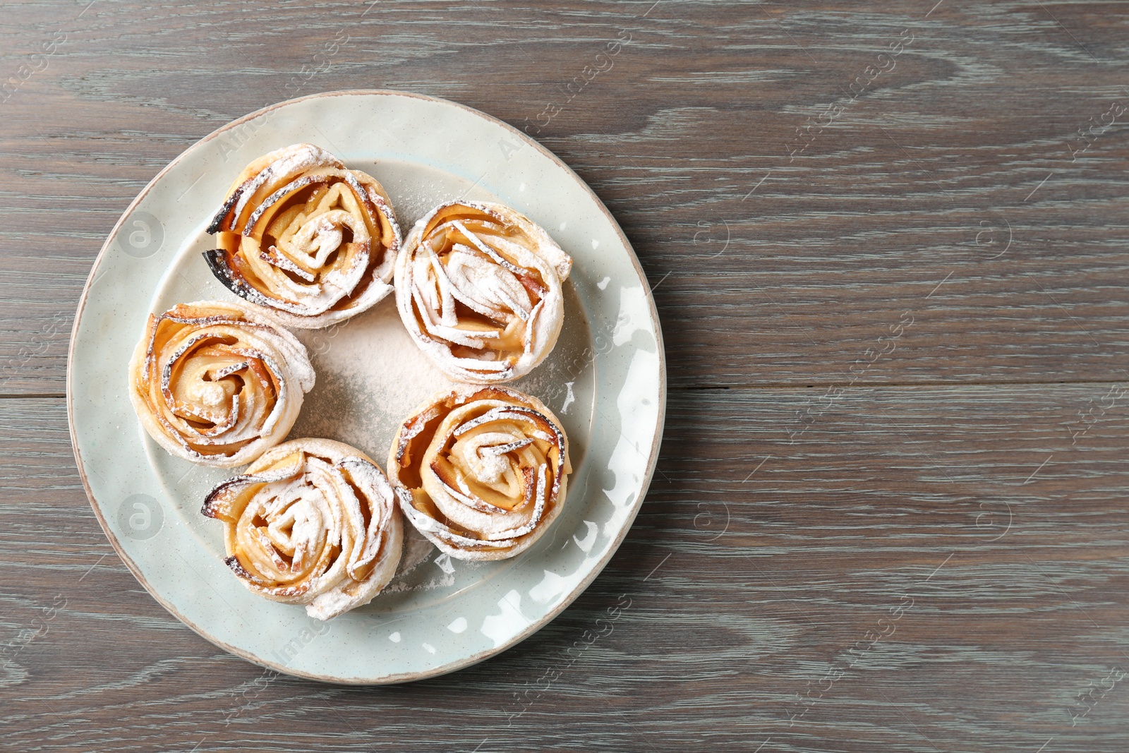 Photo of Freshly baked apple roses on wooden table, top view. Space for text