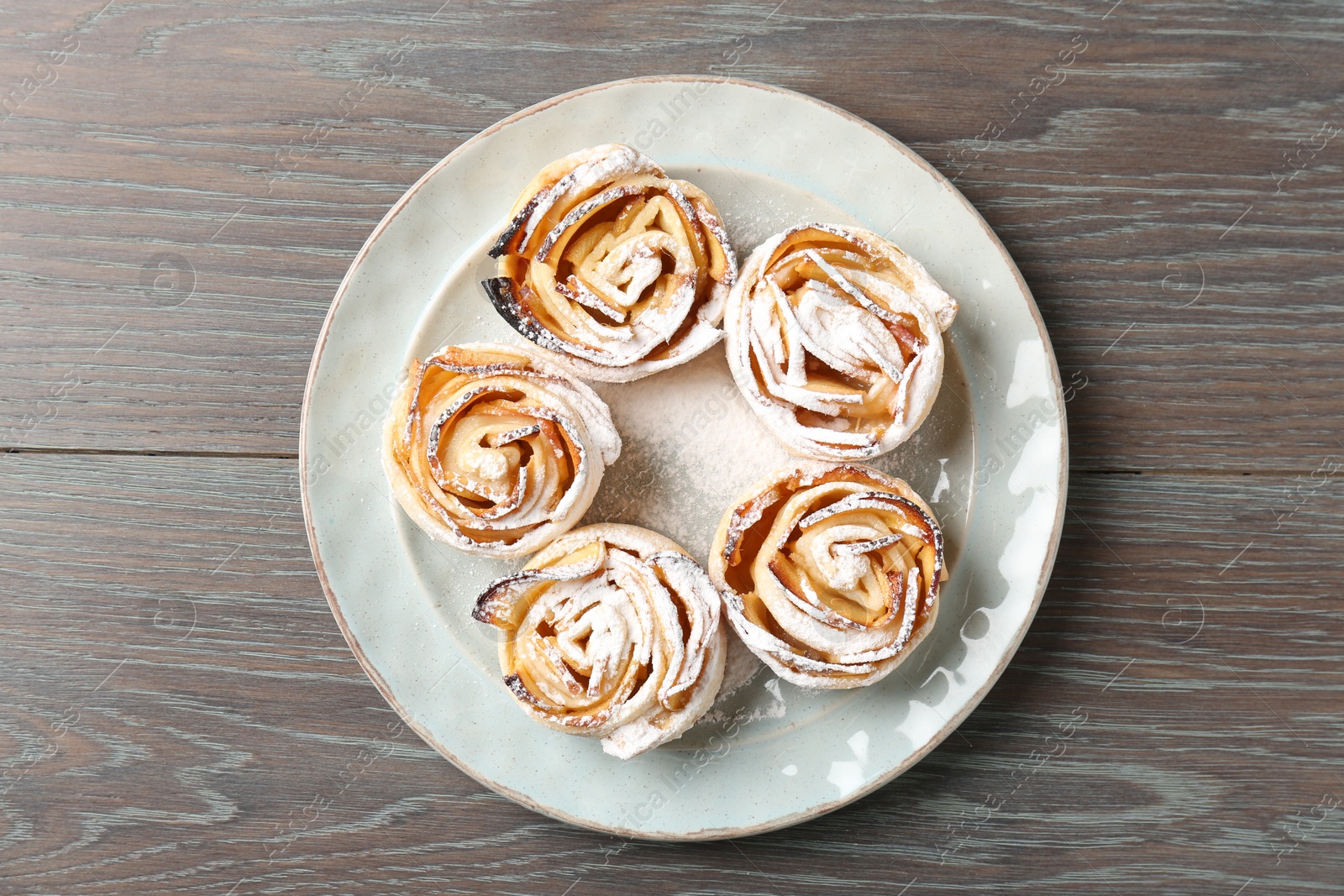 Photo of Freshly baked apple roses on wooden table, top view
