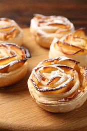 Photo of Freshly baked apple roses on wooden board, closeup