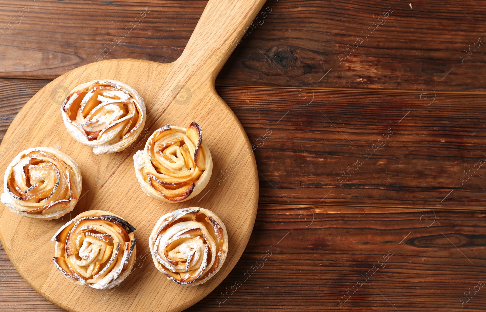 Photo of Freshly baked apple roses on wooden table, top view. Space for text