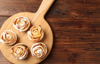 Photo of Freshly baked apple roses on wooden table, top view. Space for text