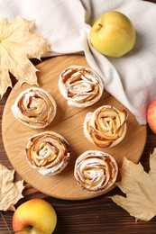 Photo of Freshly baked apple roses, fruits and dry leaves on wooden table, flat lay