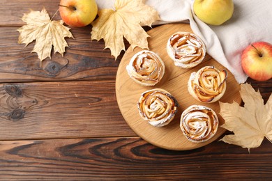 Photo of Freshly baked apple roses, fruits and dry leaves on wooden table, flat lay. Space for text