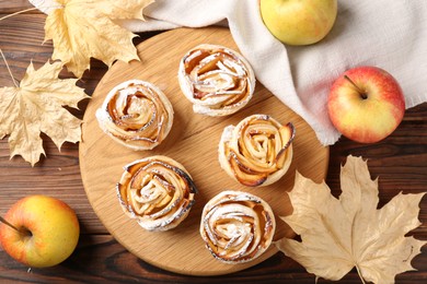 Photo of Freshly baked apple roses, fruits and dry leaves on wooden table, flat lay