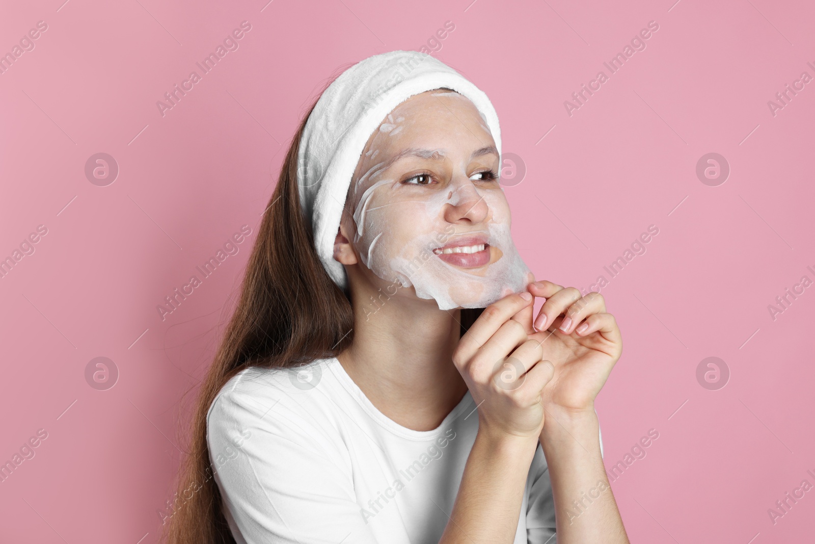 Photo of Teenage girl removing sheet facial mask on pink background. Acne treatment