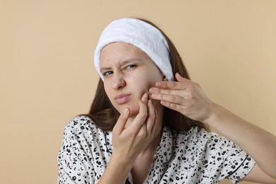 Photo of Upset teenage girl popping pimple on her face against beige background. Acne problem