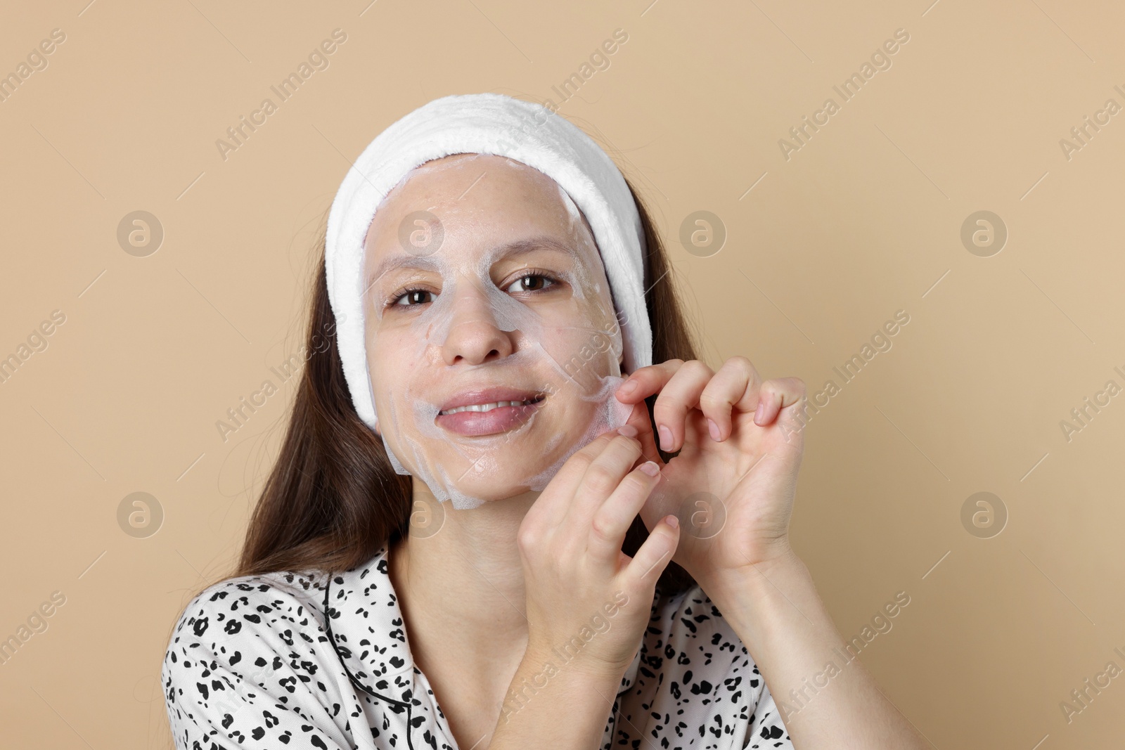 Photo of Teenage girl removing sheet facial mask on beige background. Acne treatment