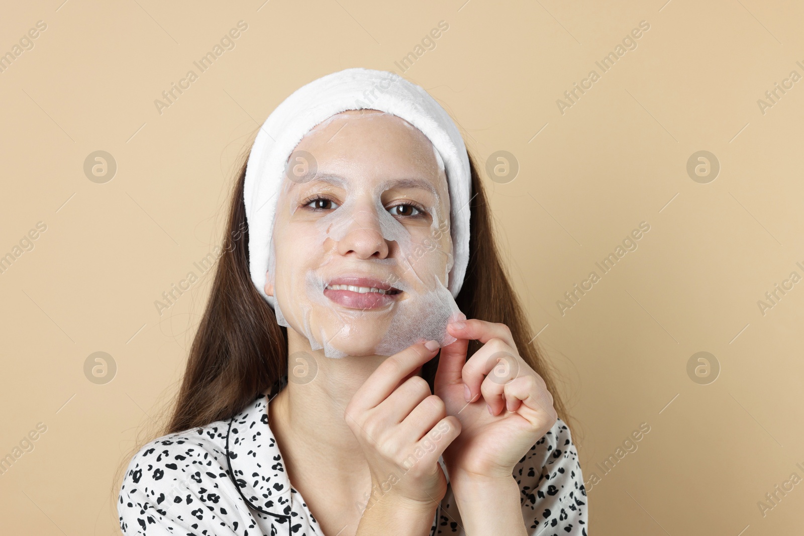 Photo of Teenage girl removing sheet facial mask on beige background. Acne treatment