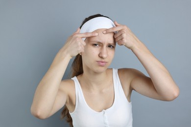 Photo of Upset teenage girl popping pimple on her face against grey background. Acne problem