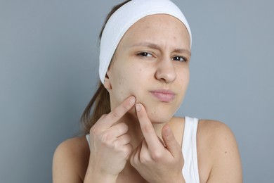 Photo of Upset teenage girl popping pimple on her face against grey background. Acne problem