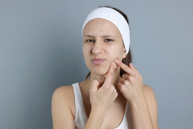 Photo of Upset teenage girl popping pimple on her face against grey background. Acne problem